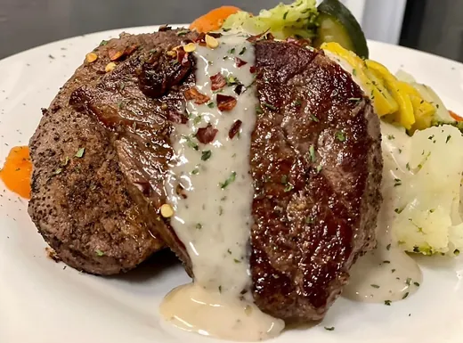 Grilled steak under cream sauce, plated with vegetables